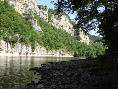 Free Stock Photo of Pebbles along the quit river surrounded by cliffs