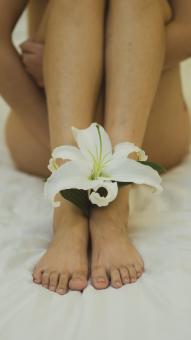 Closeup View Of Woman Holding Flower Near Legs On Bed