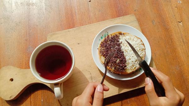 A photo of someone eating a mini martabak and drinking a cup of 
