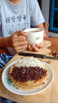 A photo of someone eating a mini martabak and drinking a cup of 