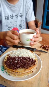 A photo of someone eating a mini martabak and drinking a cup of 