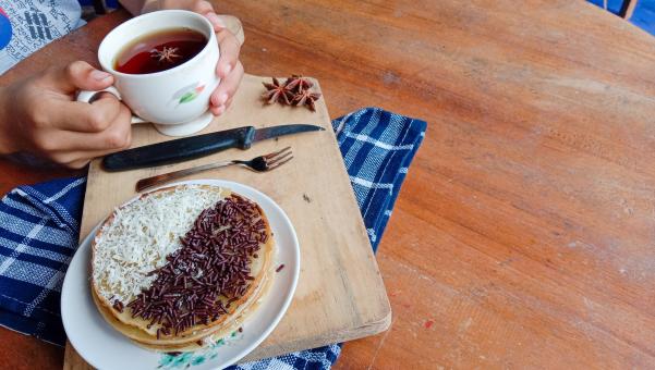 A photo of someone eating a mini martabak and drinking a cup of 
