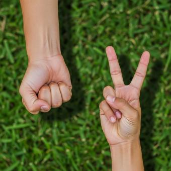 Hands playing rock paper scissors on green grass, deciding game outcom